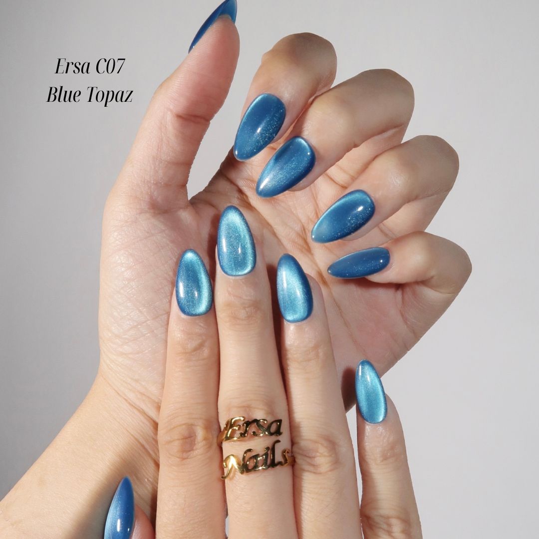 Hand with blue nail polish wearing a gold ring on a neutral background